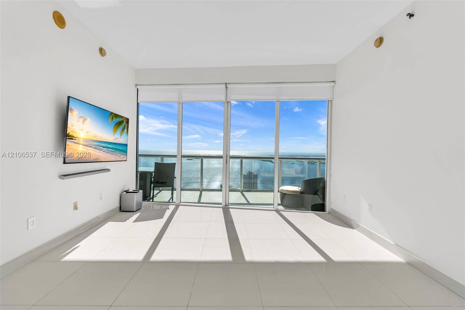 465 Brickell Avenue, #5203, Miami, FL 33131 Floor-to-ceiling glass sliding doors, large-format tile flooring, and an attached balcony with metal railing, set against a waterfront backdrop