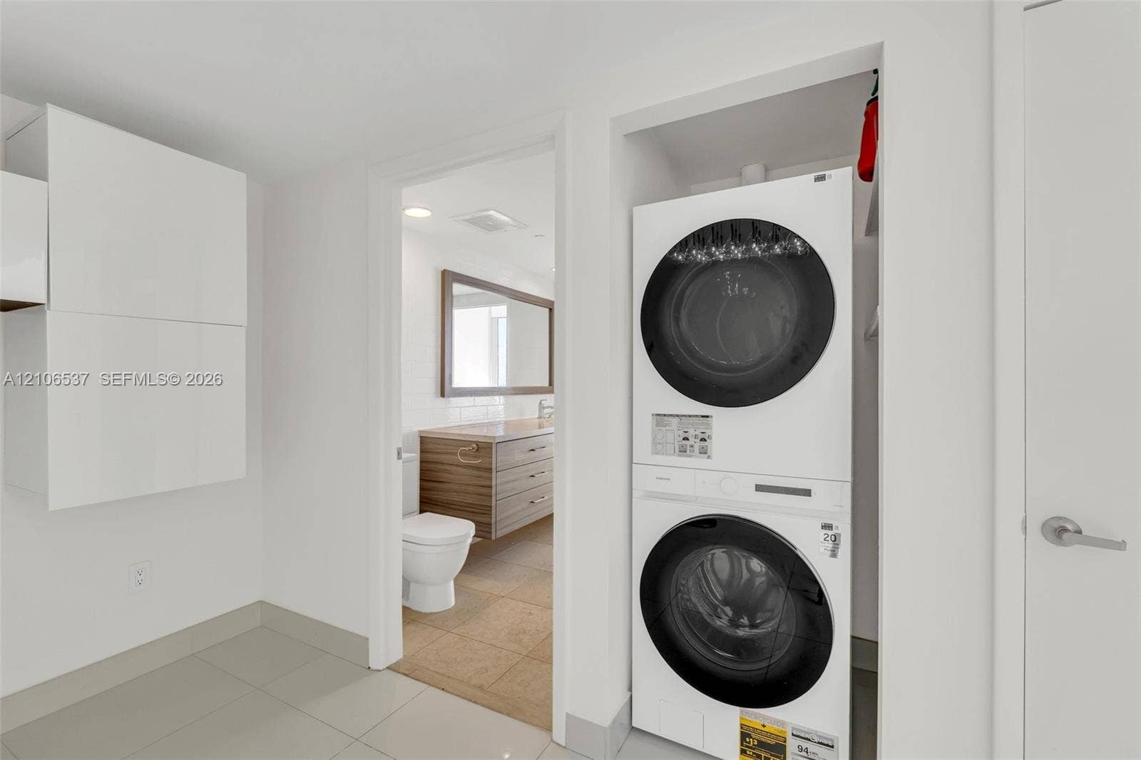 465 Brickell Avenue, #5203, Miami, FL 33131 Laundry area featuring a stacked washer and dryer unit, built-in cabinetry, ceramic tile flooring, and a doorway to a bathroom equipped with a wood-finish vanity and rectangular mirror