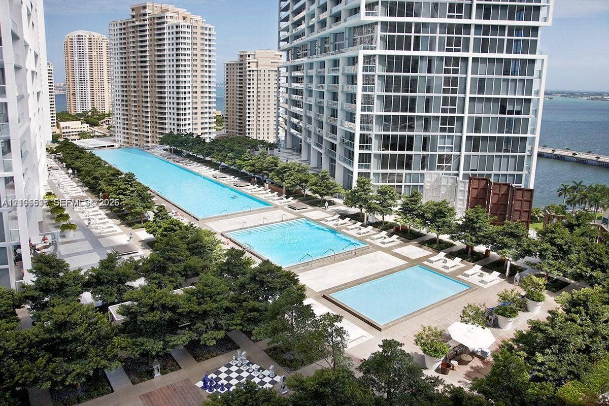 465 Brickell Avenue, #5203, Miami, FL 33131 Elevated terrace deck featuring three distinct swimming pools, manicured tree-lined landscaping, stone-finish paving, and a built-in outdoor chess board