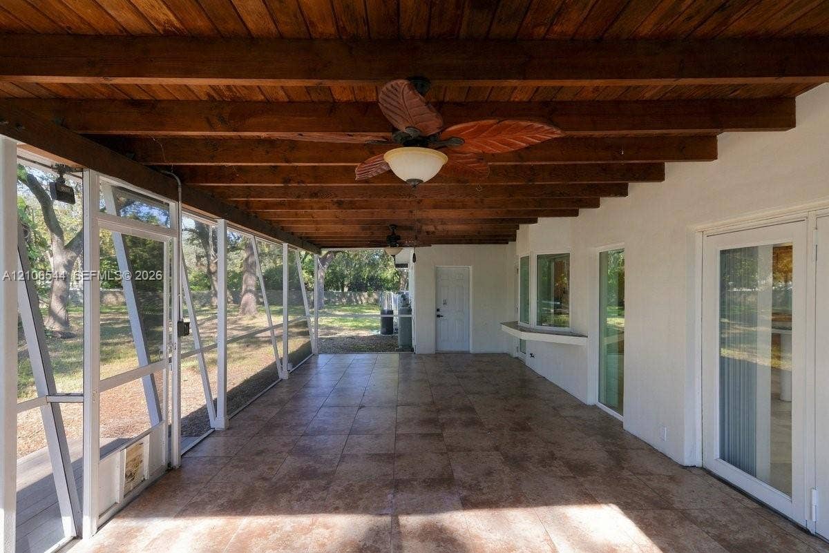 Covered patio featuring exposed wood beam ceiling, tile flooring, screen enclosure, and ceiling-mounted light fixture