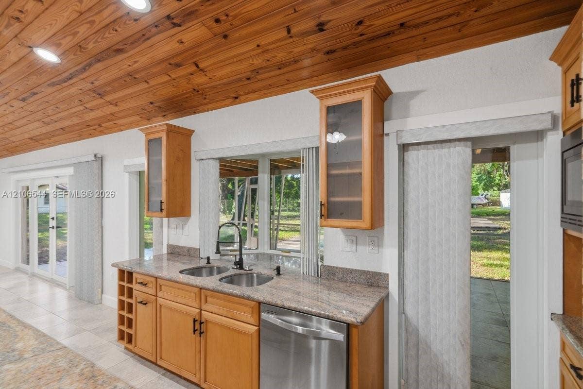 Kitchen featuring stone countertops, dual stainless steel undermount sinks, matte black faucet, natural wood-plank ceiling, and a built-in wine rack