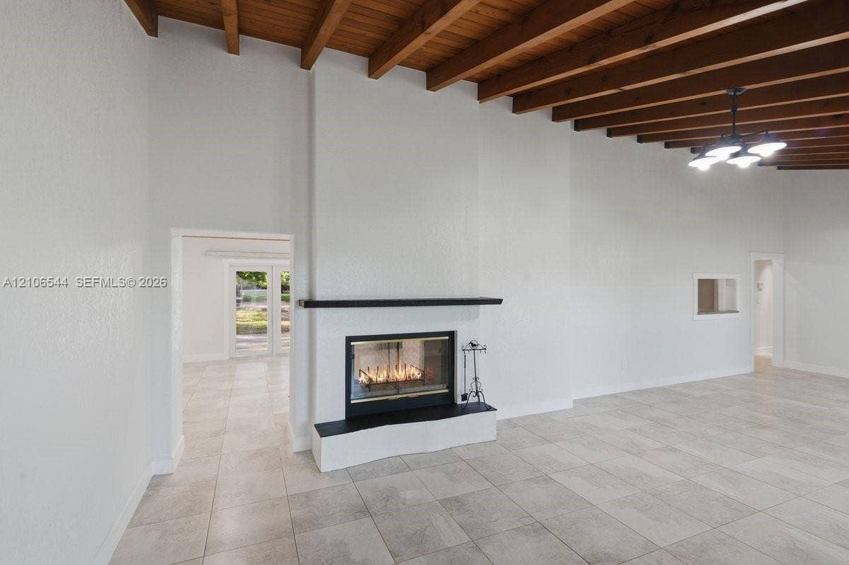 Living area featuring vaulted ceilings with exposed wood beams, large-format tile flooring, a floor-to-ceiling fireplace with a stone hearth and mantel, and a multi-arm chandelier