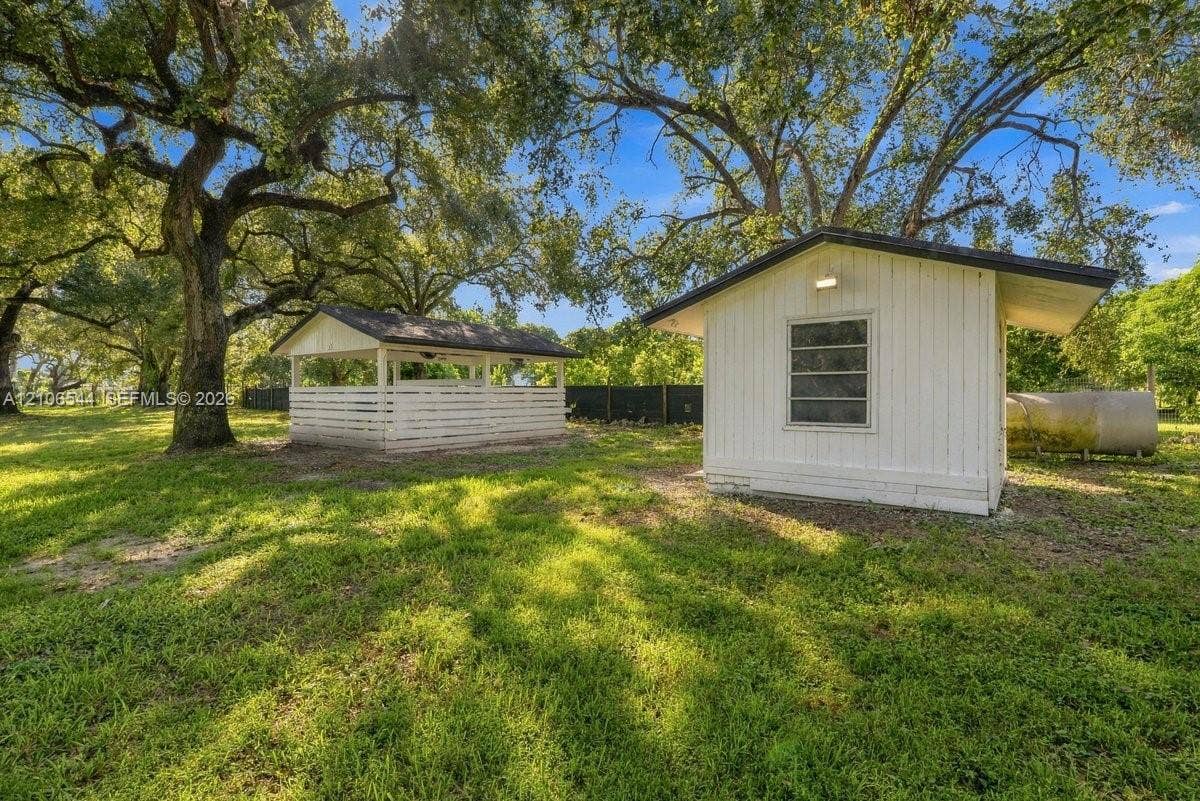 Expansive outdoor grounds featuring white-painted outbuildings, a horizontal-slat enclosure, mature canopy trees, and lawn
