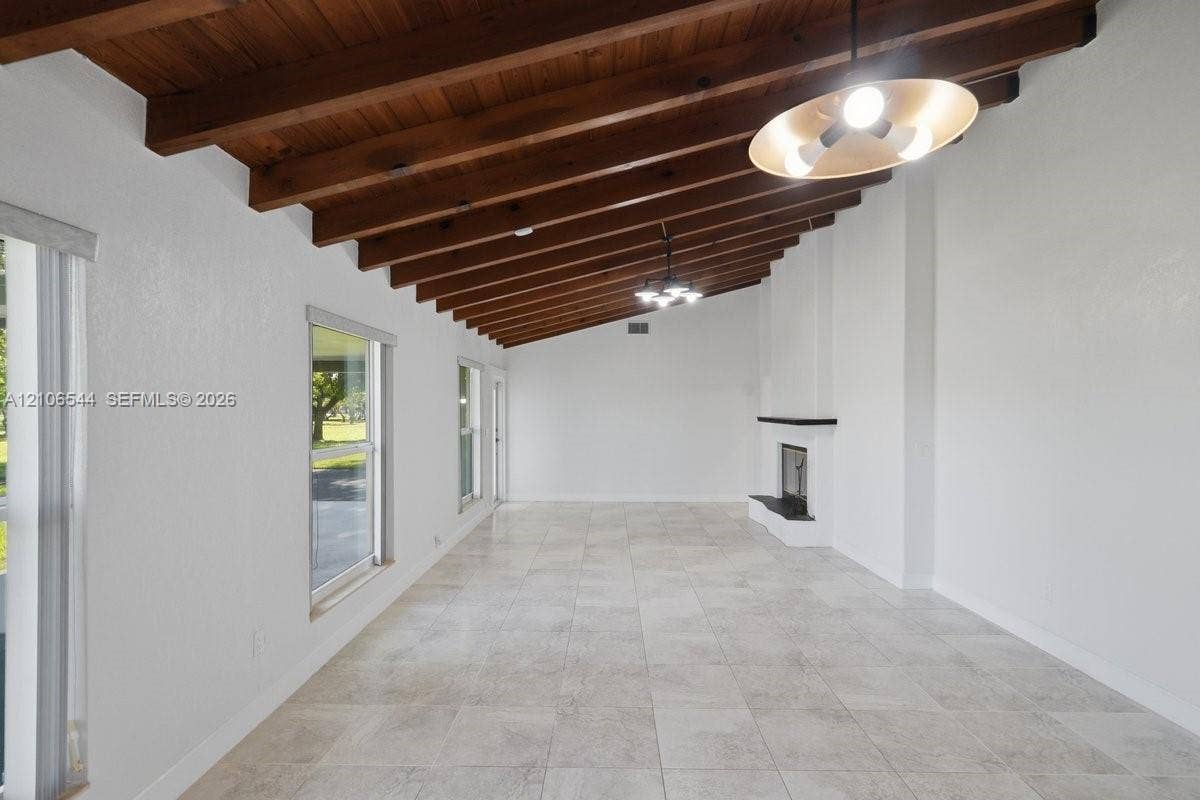 Vaulted ceiling with exposed wood beams, light-colored tile flooring, stone-surround fireplace, and multi-light pendant fixtures
