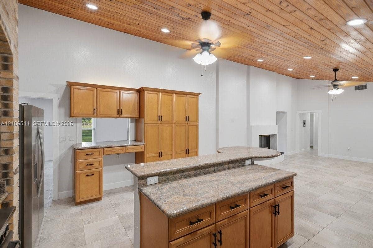 Kitchen featuring custom wood cabinetry, a stone-surround recessed cooktop area with an arched brick header, stainless steel professional-grade range, stone countertops, and a tongue-and-groove wood ceiling