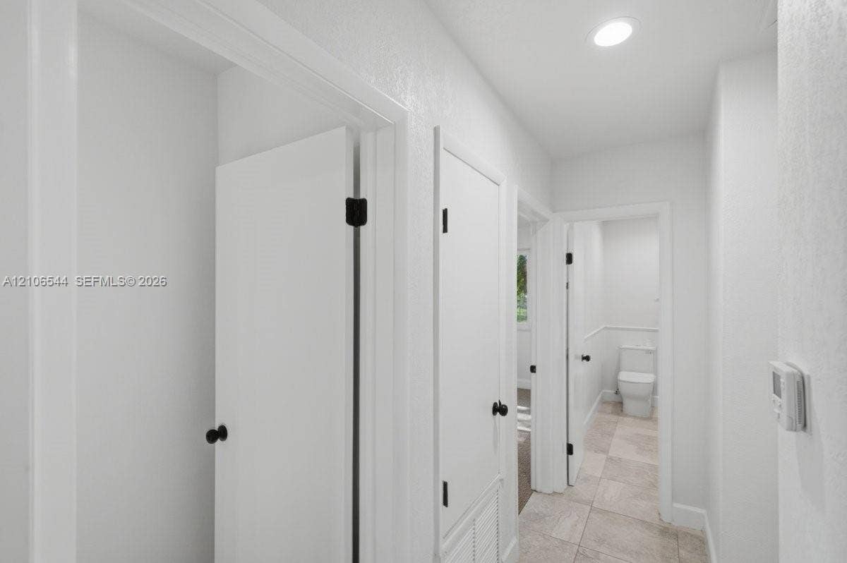 Neutral-toned interior space featuring wall-to-wall carpeting, white walls, dual windows, and a ceiling-mounted light fixture with a multi-blade fan
