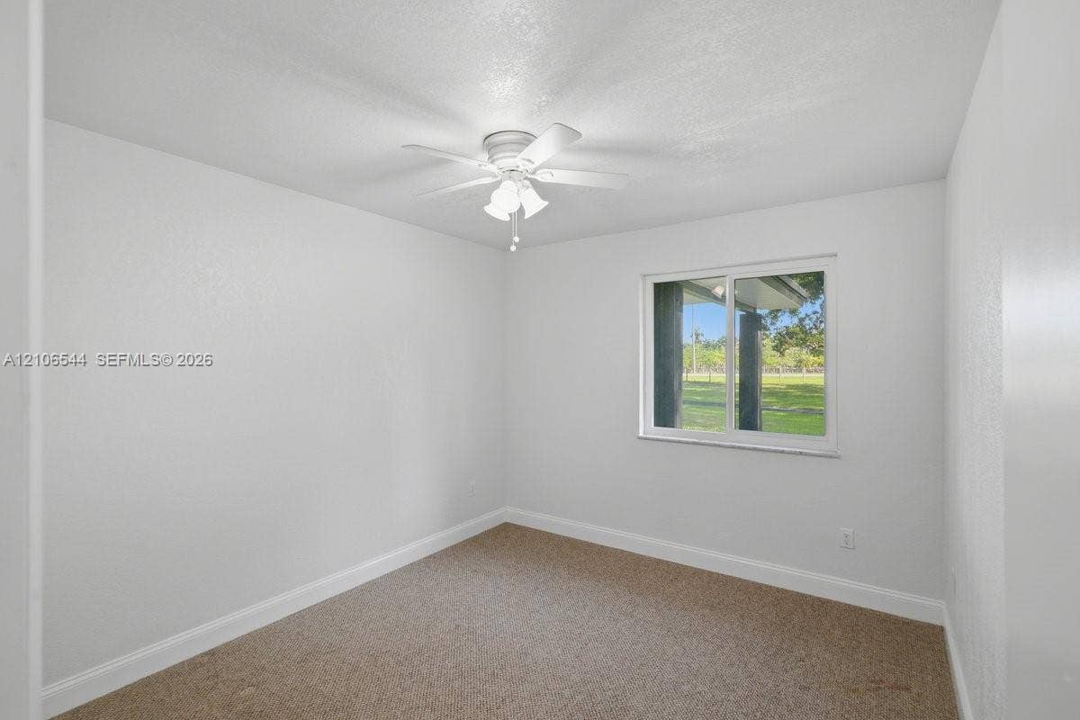 Neutral-toned interior space featuring neutral carpeting, a white ceiling fan with integrated lighting, and a single-pane horizontal sliding window