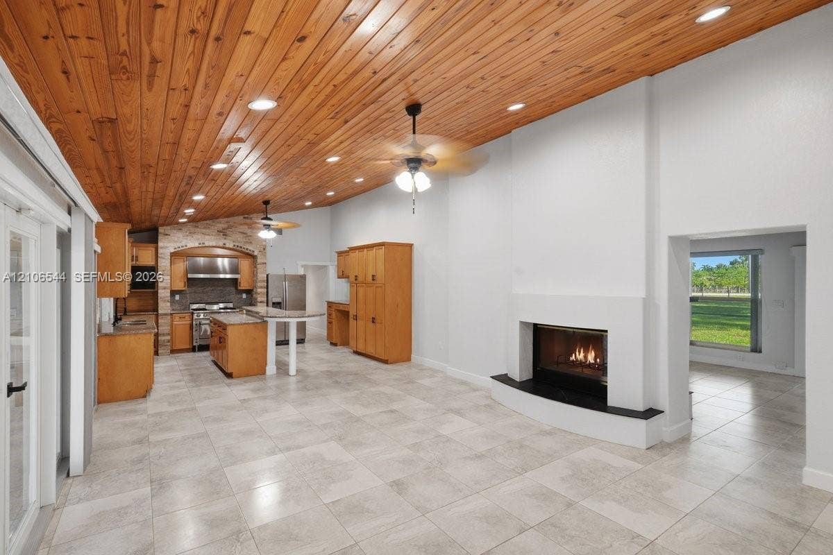 Vaulted wood-plank ceiling, neutral tile flooring, recessed lighting, double glass-panel doors, and built-in cabinetry with stone-finish countertops