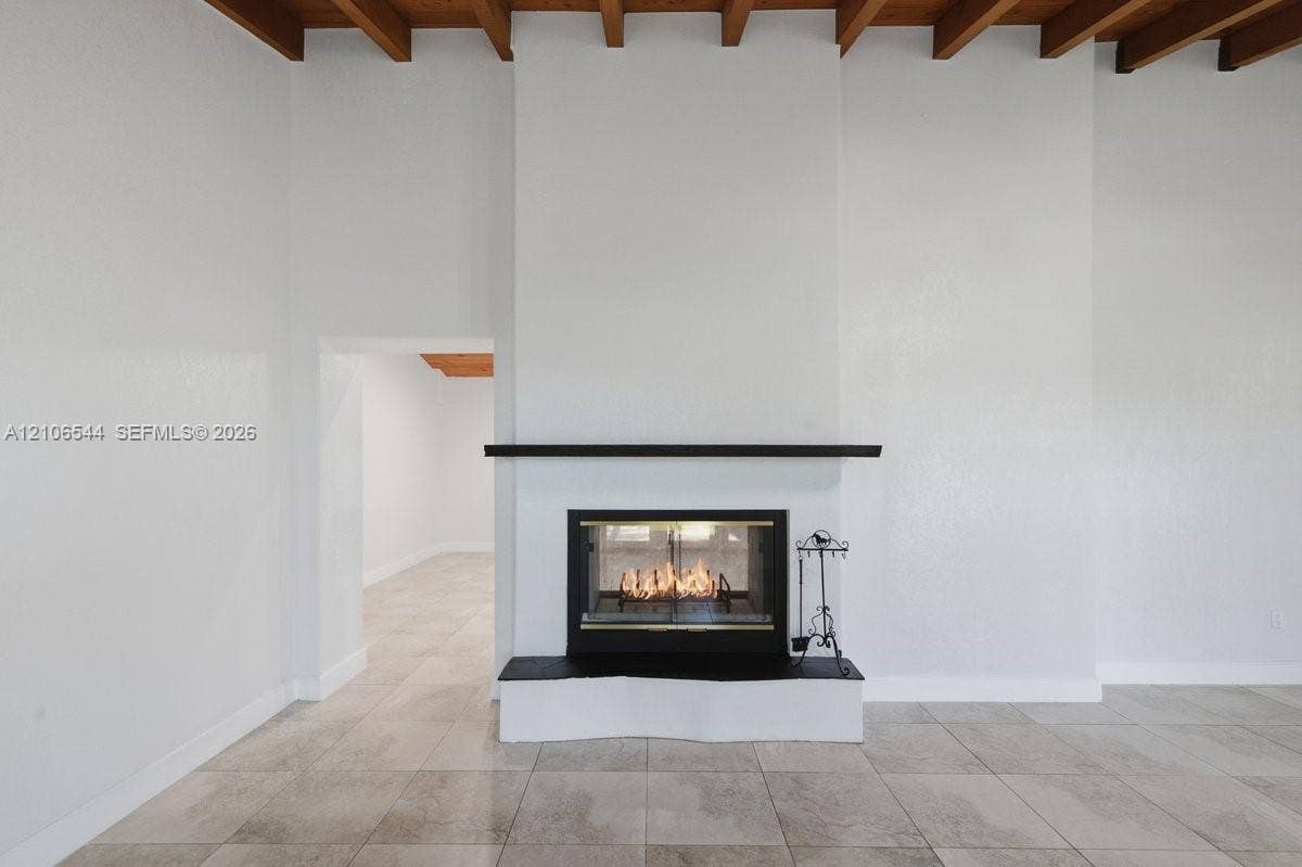 Living area featuring vaulted ceilings with exposed wood beams, large-format tile flooring, a floor-to-ceiling fireplace with a stone hearth and mantel, and a multi-arm chandelier