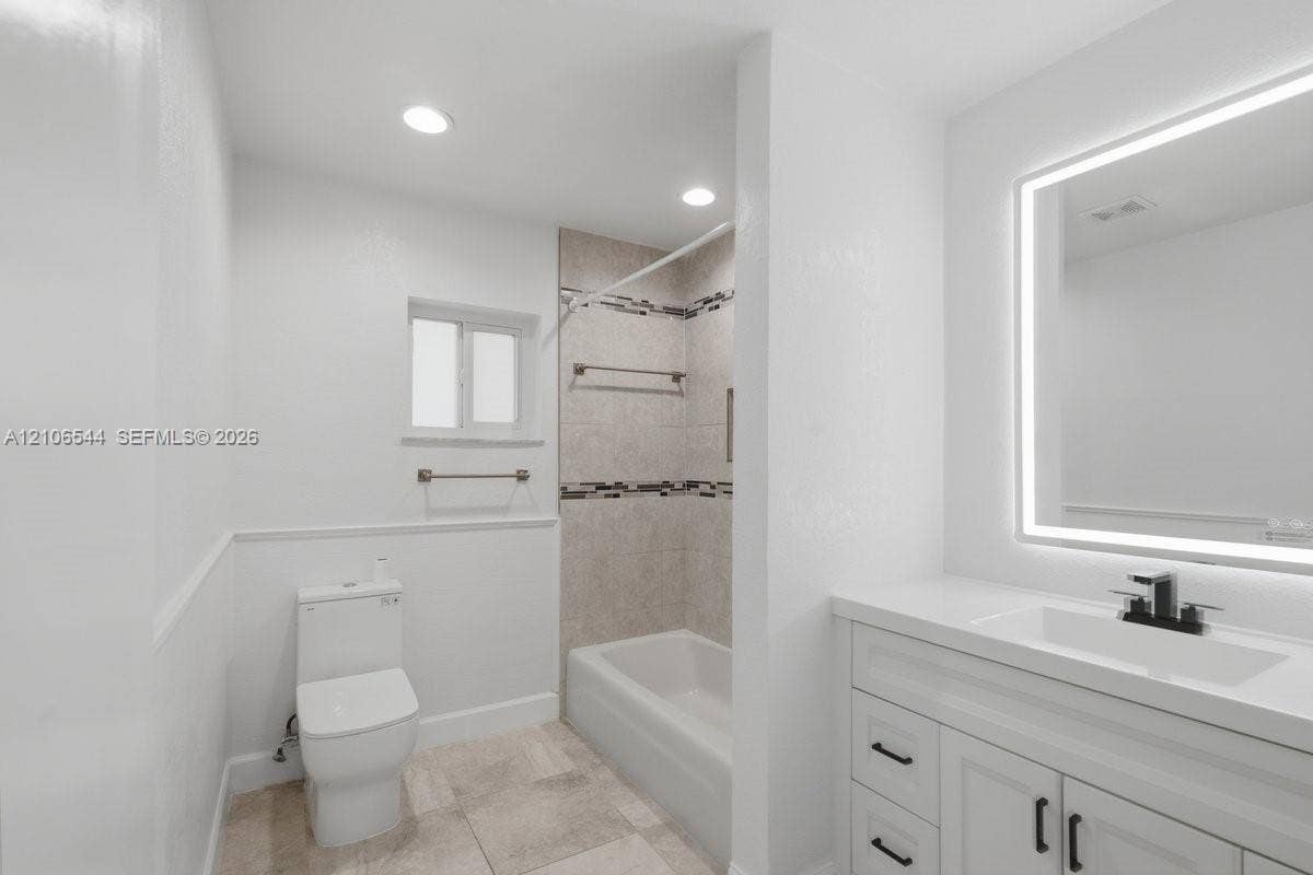 Tiled shower featuring a decorative mosaic inlay, handheld shower head, white vanity with cabinetry, and an integrated LED mirror