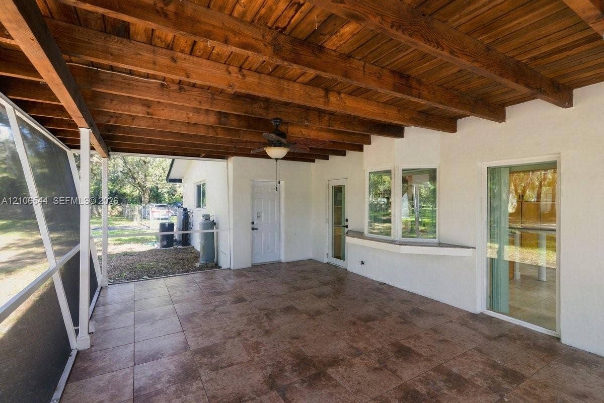 Screened-in patio featuring tile flooring, exposed wood-beam ceiling, ceiling fans, and structural metal support columns