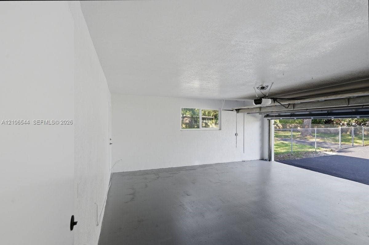 Two-car garage featuring painted concrete flooring, smooth interior walls, an installed ceiling-mounted garage door opener, and a single-pane window