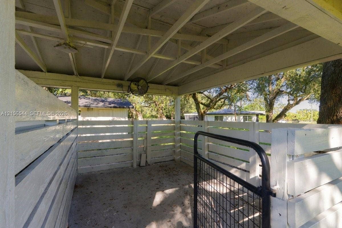 Outbuilding with white vertical siding, pitched roof, and concrete pad situated on an expansive lot with mature trees