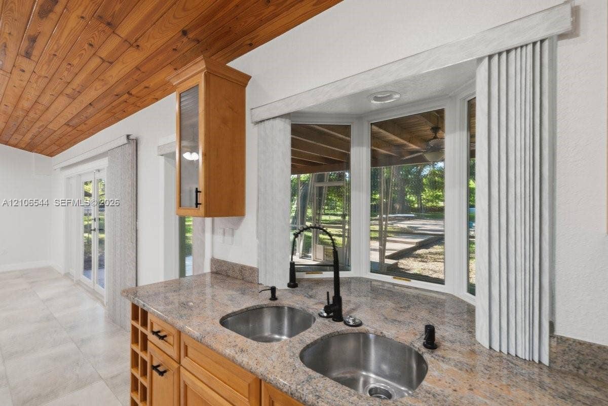 Kitchen featuring stone countertops, dual stainless steel undermount sinks, matte black faucet, natural wood-plank ceiling, and a built-in wine rack