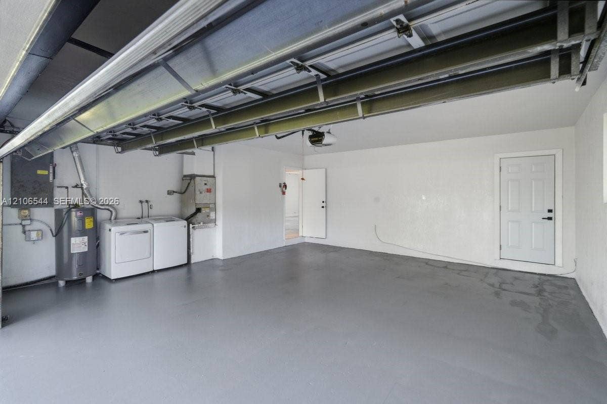 Garage interior featuring painted flooring, overhead door mechanism, integrated water heater, and a dedicated utility area with built-in laundry hookups