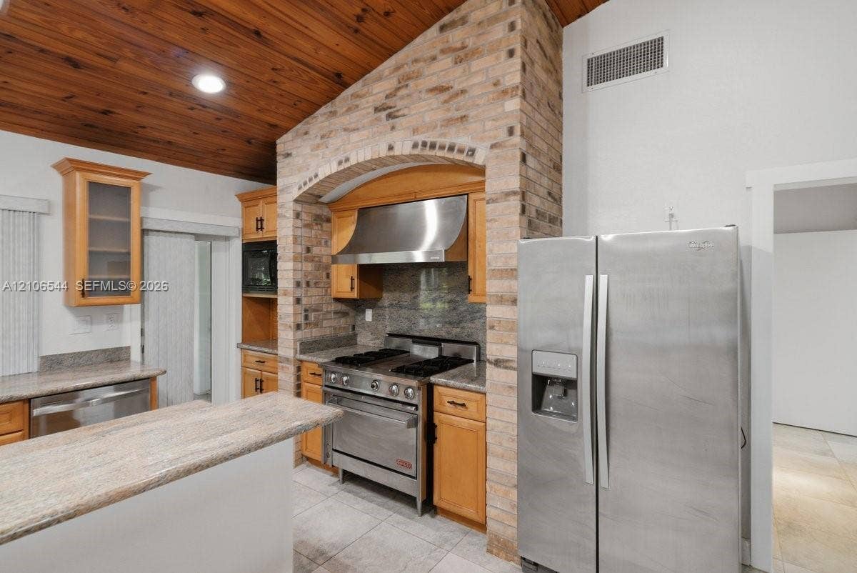 Kitchen featuring a vaulted wood-plank ceiling, recessed lighting, stone-finish countertops, stainless steel dual-basin sink with a matte black faucet, and natural wood cabinetry with glass-panel doors