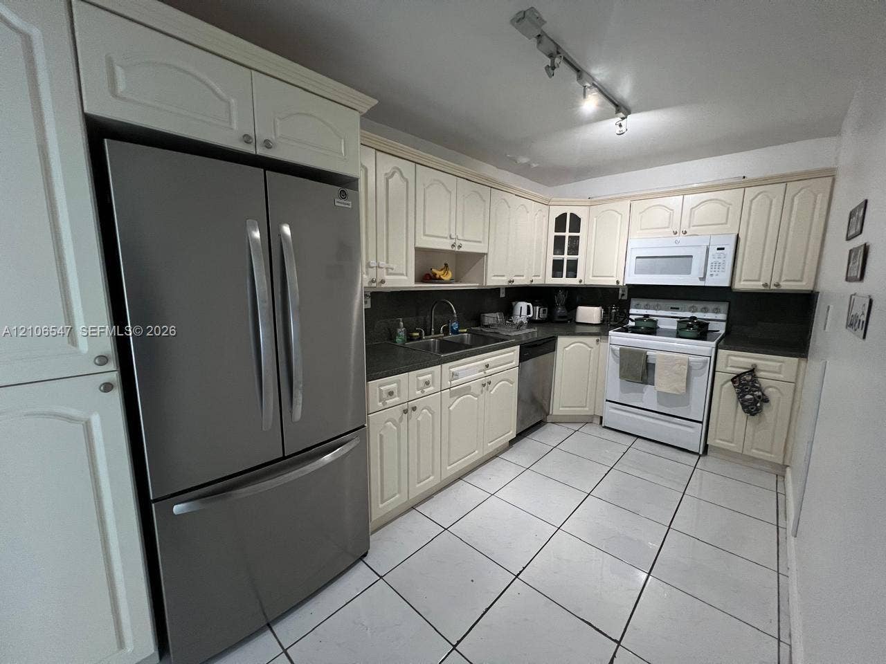 6801 Indian Creek Drive, #509, Miami Beach, FL 33141 Kitchen featuring off-white cabinetry, stainless steel French-door refrigerator, dark solid-surface countertops, white tile flooring, and track lighting