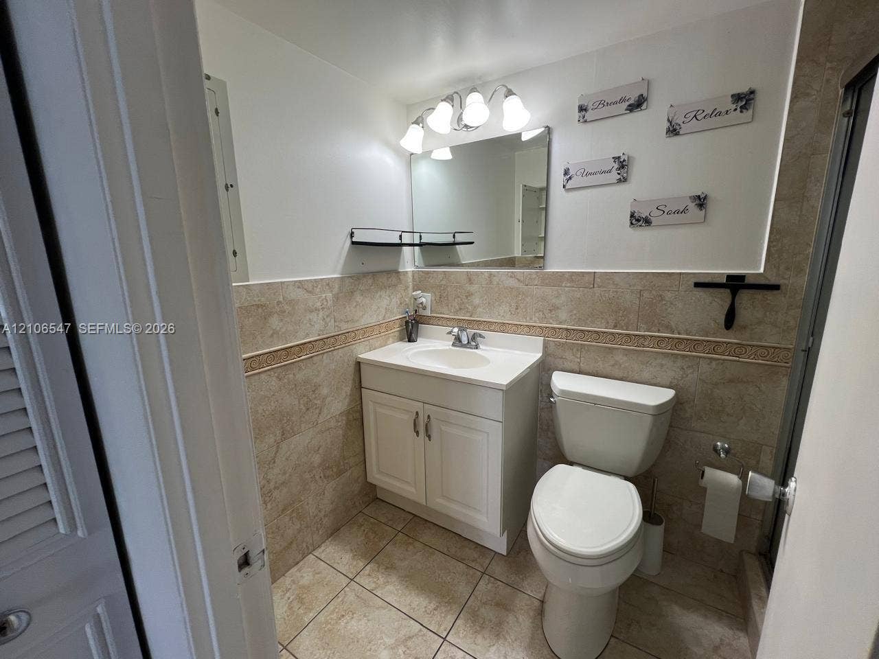 6801 Indian Creek Drive, #509, Miami Beach, FL 33141 Bathroom featuring stone-finish wall and floor tile with decorative border, white cabinet vanity with integrated sink, four-light vanity fixture, and rectangular wall mirror