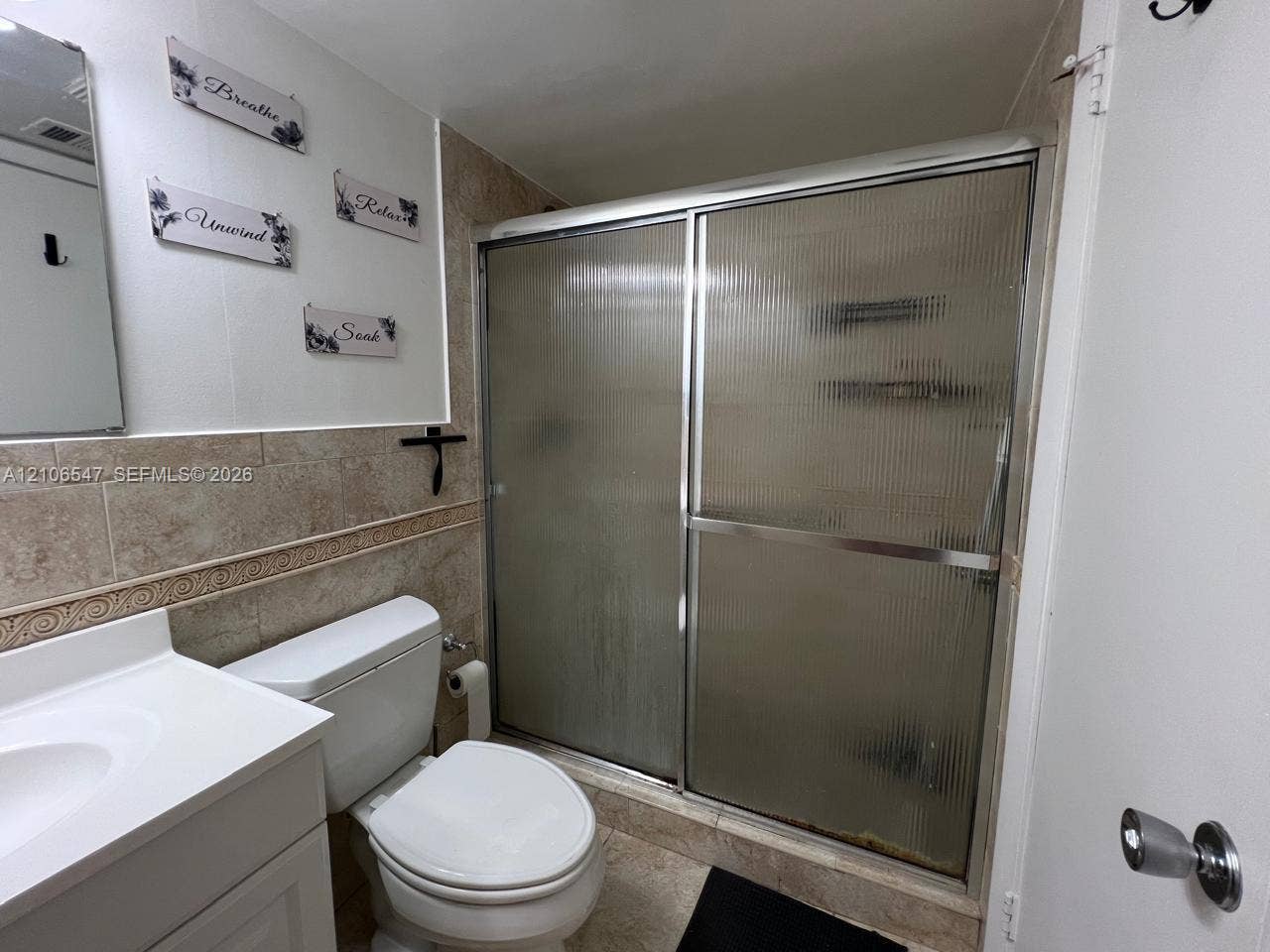 6801 Indian Creek Drive, #509, Miami Beach, FL 33141 Bathroom featuring a white vanity with an integrated basin, a standard toilet, and a walk-in shower enclosed by reeded glass sliding doors with metallic framing, finished with wall-to-wall ceramic tile surround and coordinating floor tile