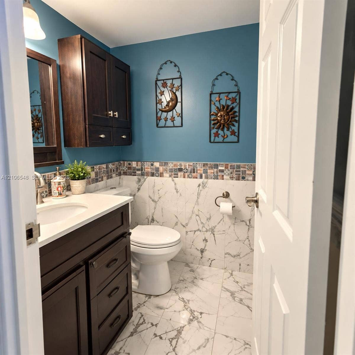 Dark-toned wooden vanity featuring built-in cabinetry and a white countertop, complemented by large-format veined floor and wall tile, mosaic tile backsplash, and wall-mounted brushed metal hardware
