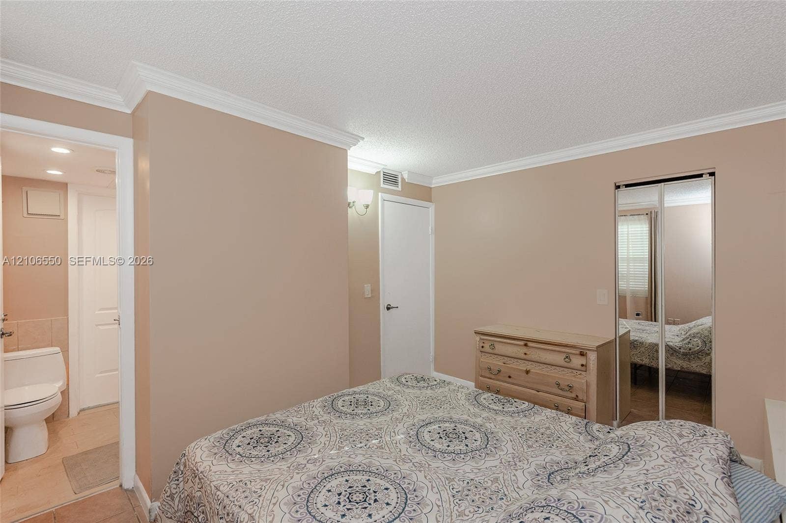 Room featuring crown molding, neutral wall finishes, a closet with mirrored sliding doors, and an entry to a full bathroom equipped with a toilet