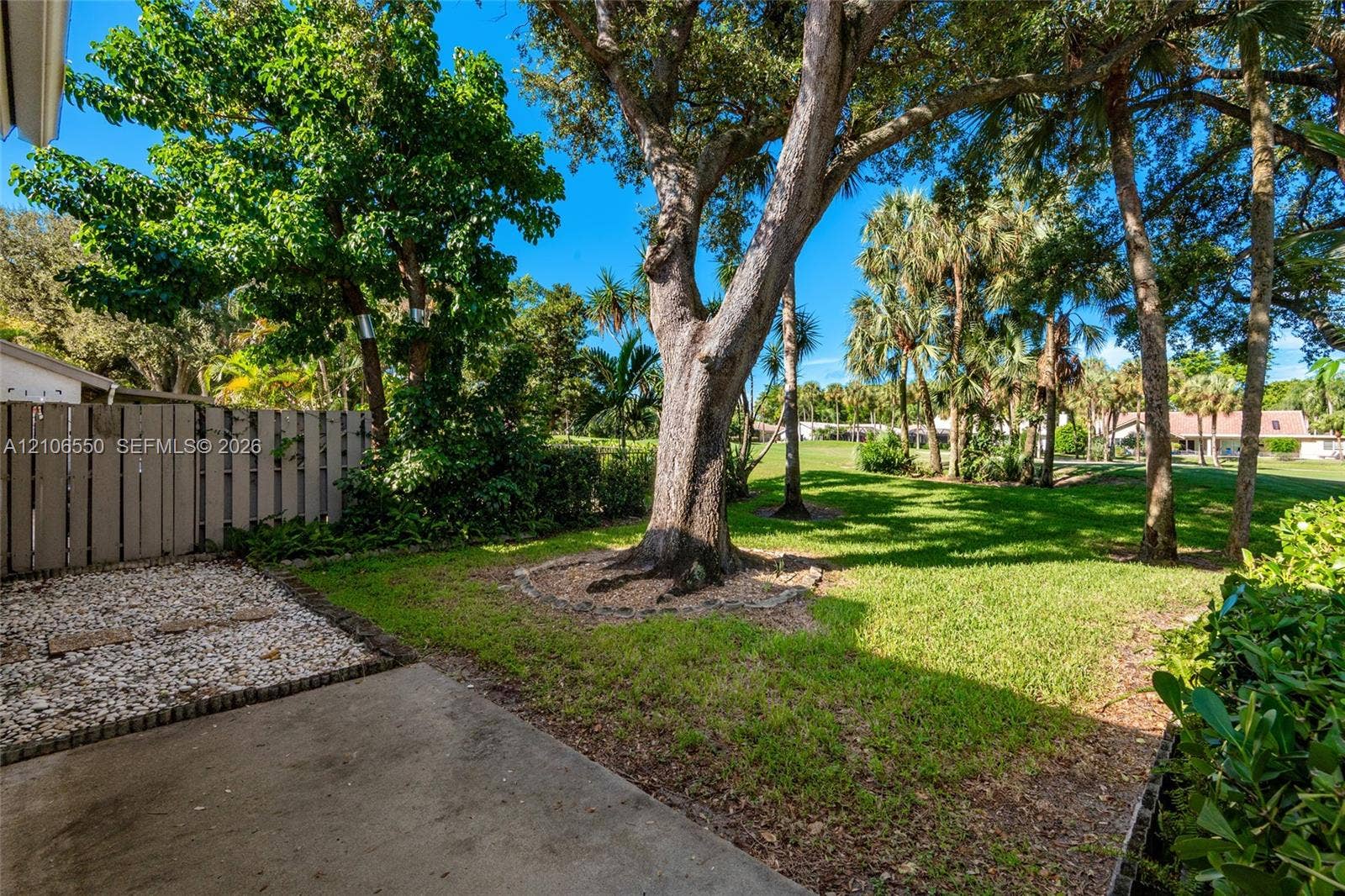 Backyard featuring a concrete patio, gravel border, vertical wood-slat privacy fencing, mature trees, and landscaped grass area