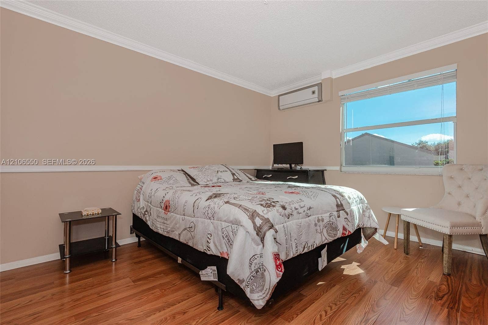 Bedroom featuring wood-finish flooring, wall-mounted climate control unit, chair rail molding, and large window with horizontal blinds