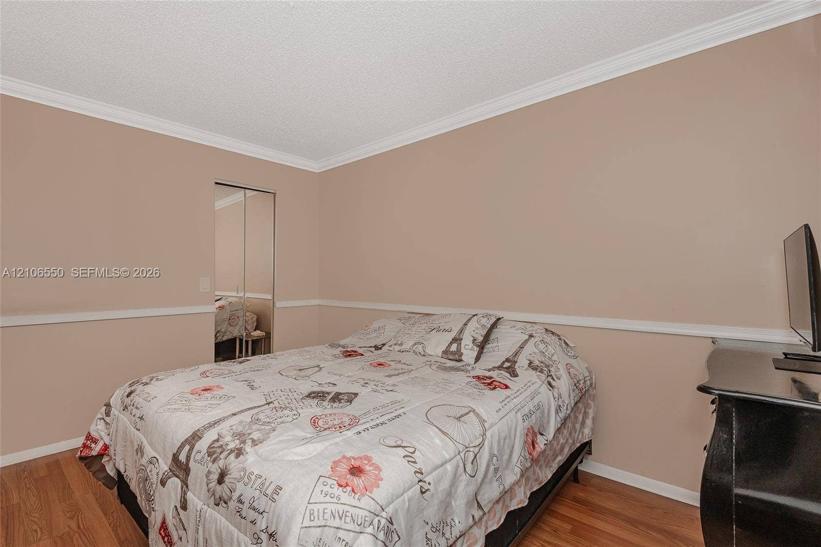 Room featuring wood-finish flooring, crown molding, chair rail trim, and mirrored sliding closet doors