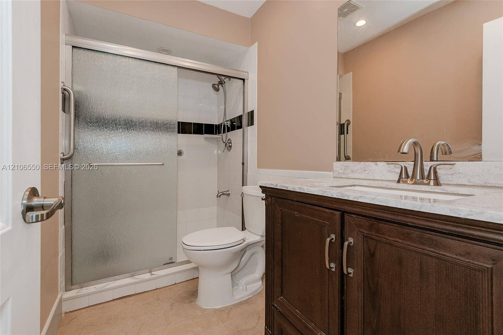 Bathroom featuring a dark wood vanity with a stone-finish countertop, undermount sink, shower with sliding glass doors, and a frameless wall mirror