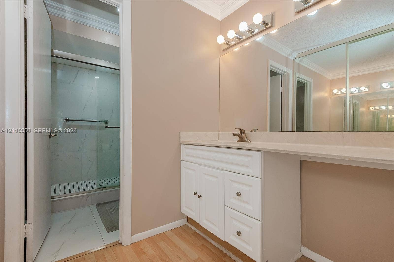 Bathroom vanity featuring a white cabinet base, stone-look countertop, integrated sink, and full-width wall mirror with attached multi-bulb lighting
