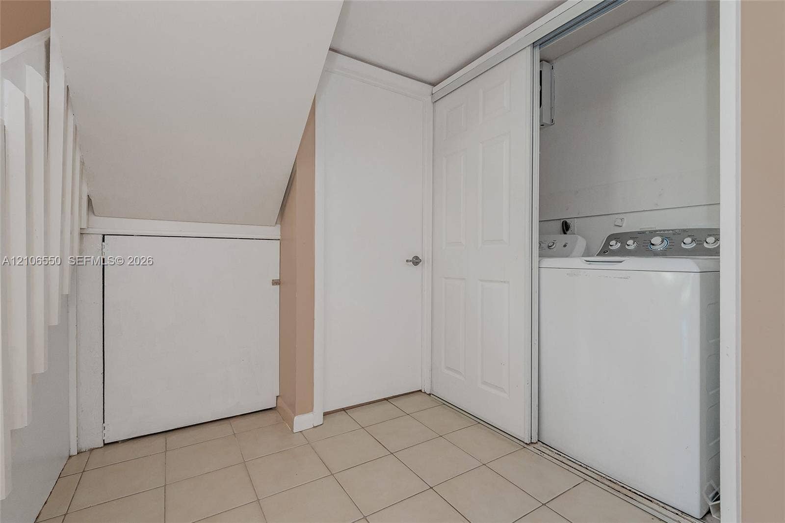 Laundry area featuring tile flooring, a dedicated closet with sliding doors, and under-stair storage cabinetry