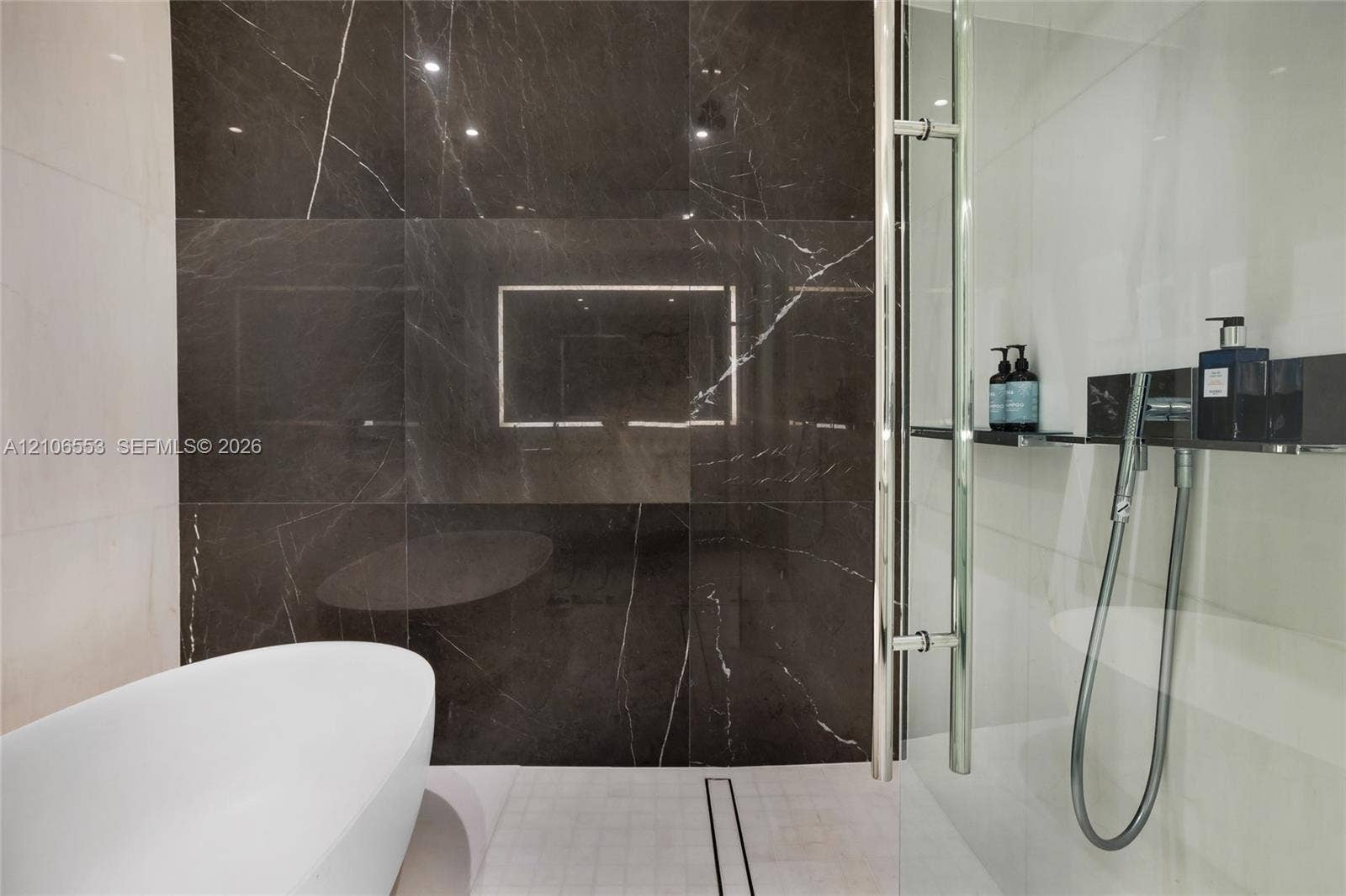 300 Biscayne Boulevard Way, #3002E, Miami, FL 33131 Freestanding soaking tub, floor-to-ceiling dark stone-finish wall tile, and glass-enclosed shower with polished chrome fixtures and an integrated shelf