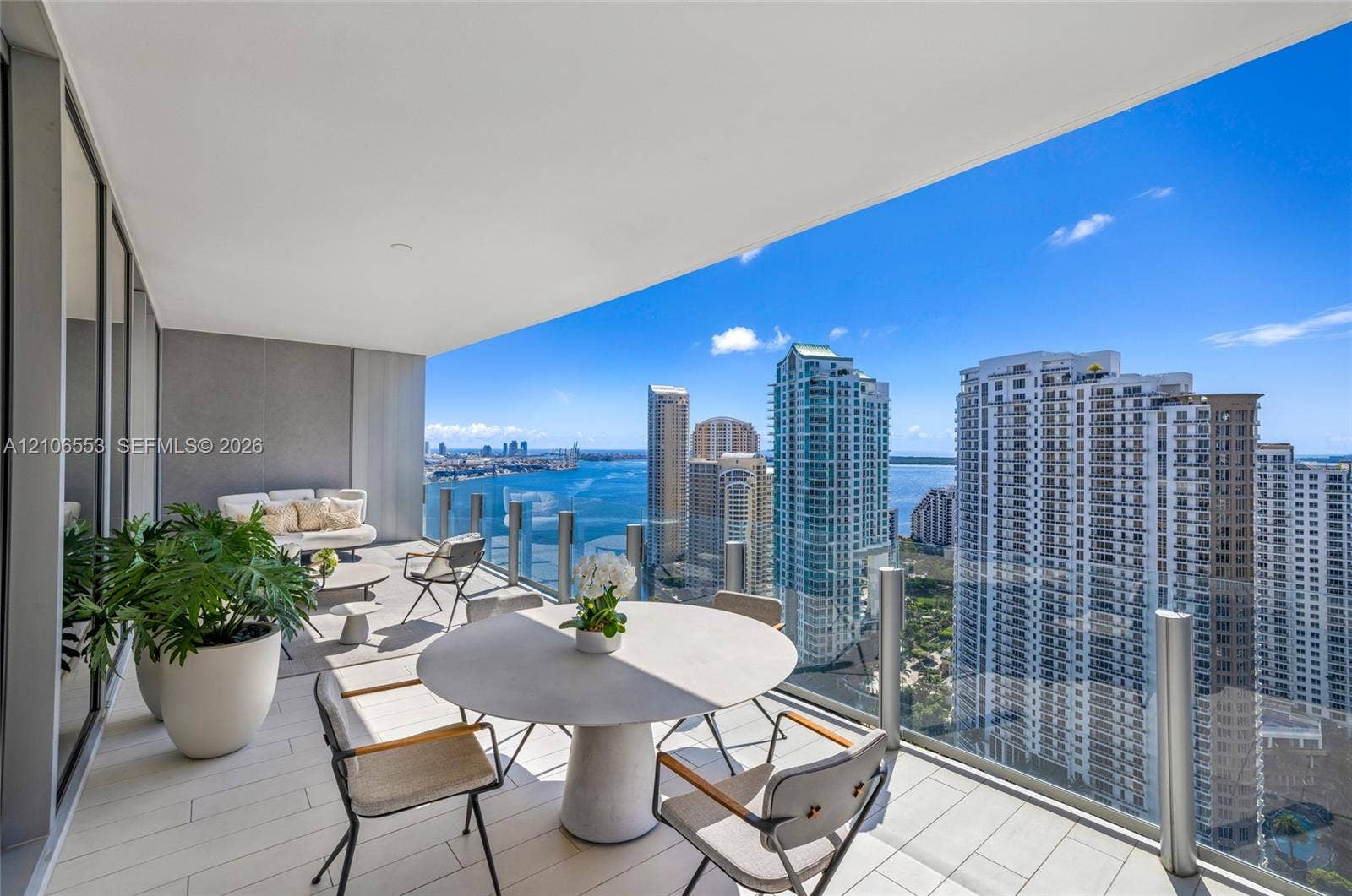 300 Biscayne Boulevard Way, #3002E, Miami, FL 33131 Expansive covered balcony with large-format tile flooring and a glass railing, showcasing a panorama of the surrounding urban skyline and water