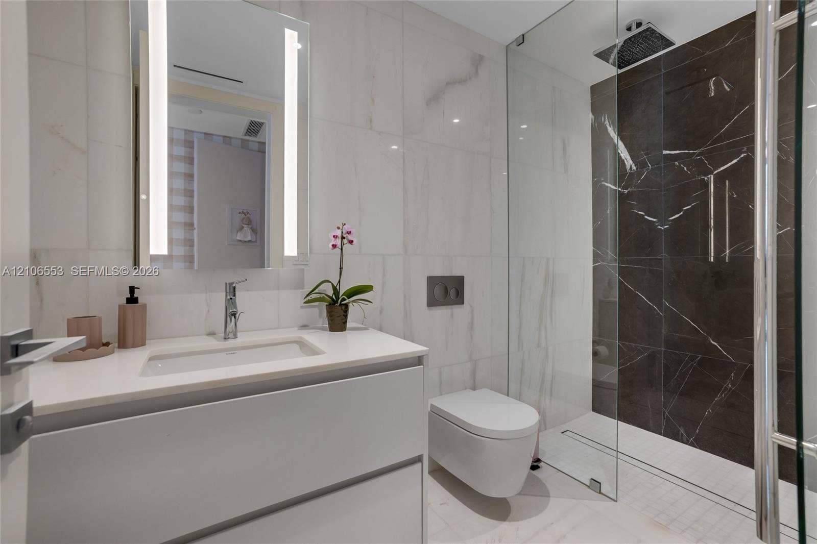300 Biscayne Boulevard Way, #3002E, Miami, FL 33131 Floating vanity with a quartz countertop, integrated rectangular sink, wall-mounted dual-flush toilet, glass-enclosed shower with dark stone-finish tiling, and a backlit vanity mirror
