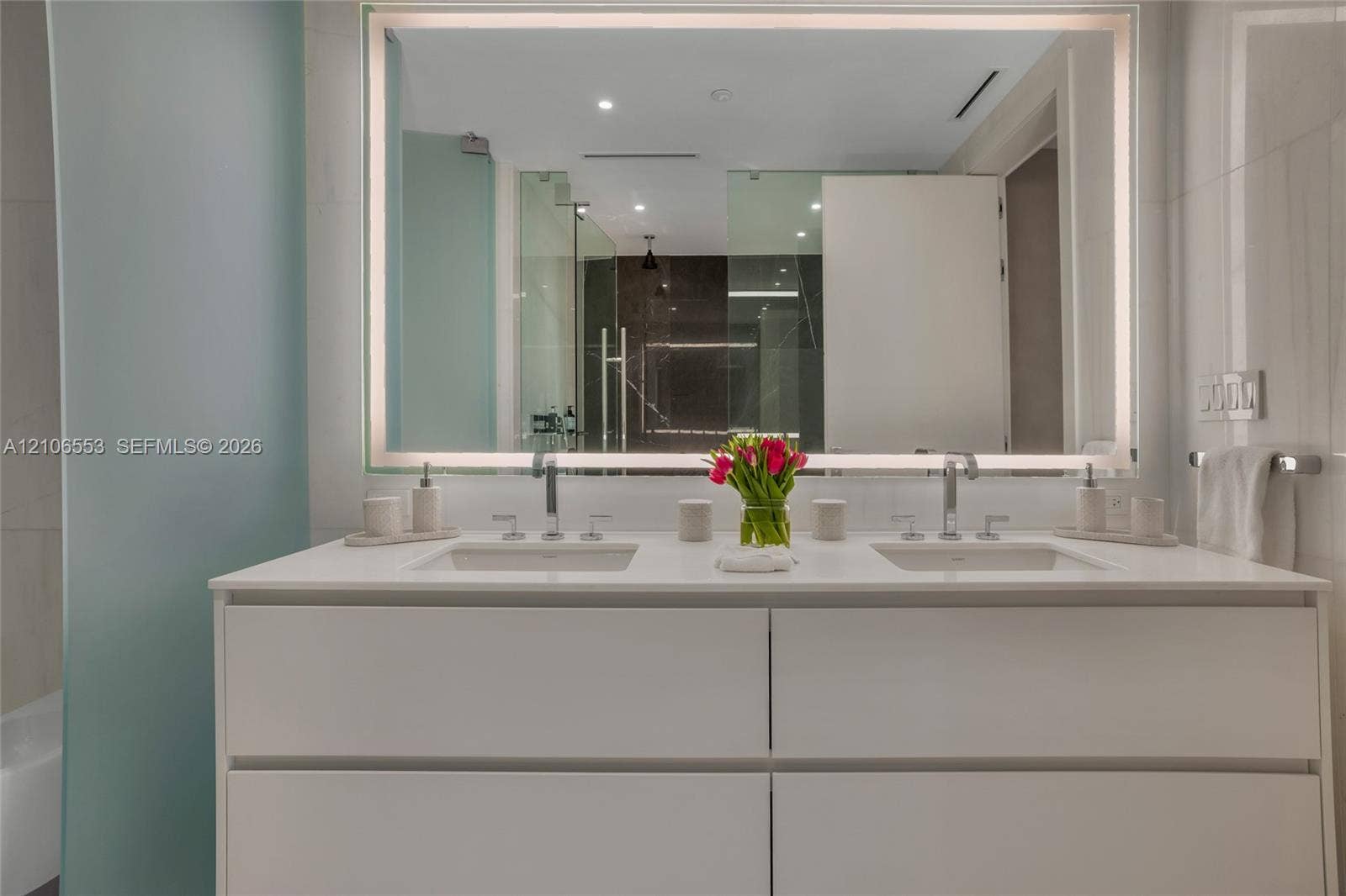300 Biscayne Boulevard Way, #3002E, Miami, FL 33131 Double vanity featuring a white cabinetry base, dual undermount sinks, stone countertops, wall-mounted chrome faucets, and an expansive integrated LED-backlit mirror