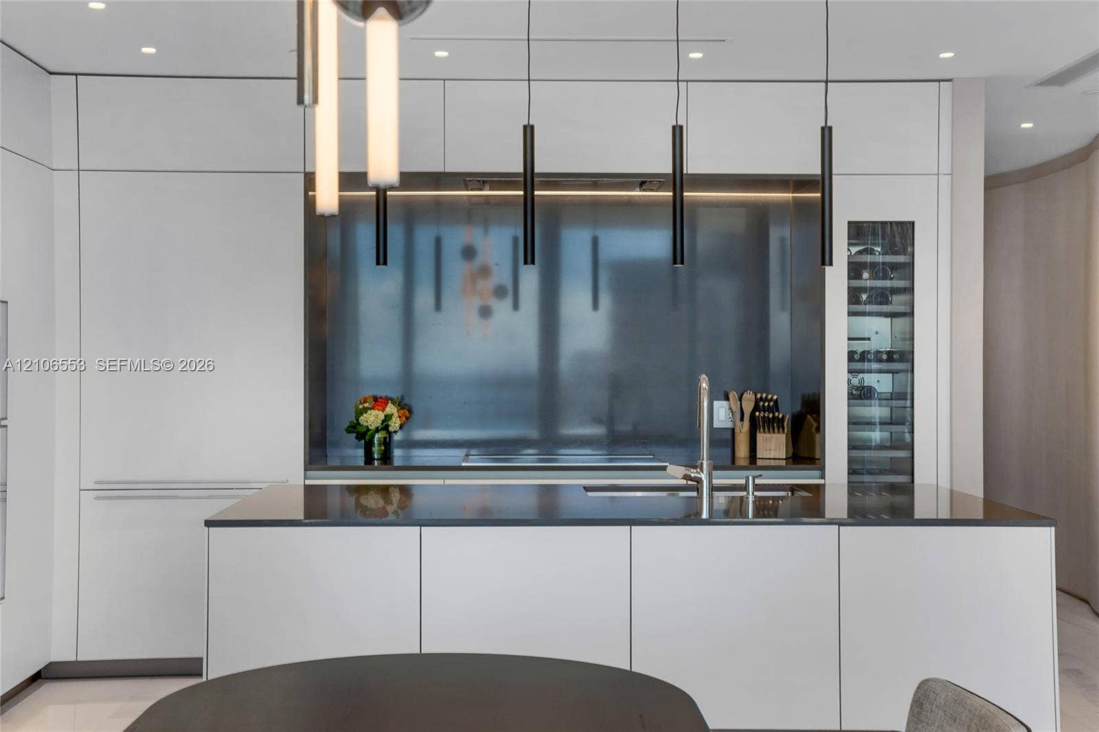300 Biscayne Boulevard Way, #3002E, Miami, FL 33131 Minimalist kitchen featuring flat-panel cabinetry, a stainless steel backsplash, an integrated wine refrigerator, linear pendant lighting, and a solid-surface island with a built-in sink