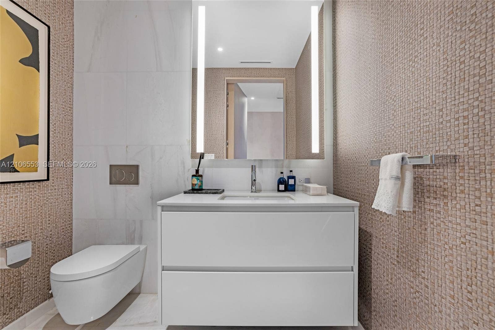 300 Biscayne Boulevard Way, #3002E, Miami, FL 33131 Floating vanity with a smooth white finish and countertop basin, wall-mounted commode, integrated vertical LED mirror lighting, and textured wall tile