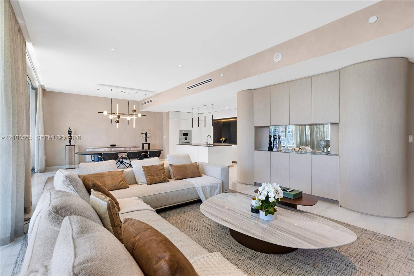 300 Biscayne Boulevard Way, #3002E, Miami, FL 33131 Open-concept living space featuring floor-to-ceiling windows, light-toned stone-finish flooring, custom curved built-in cabinetry, recessed lighting, and a modern multi-light chandelier