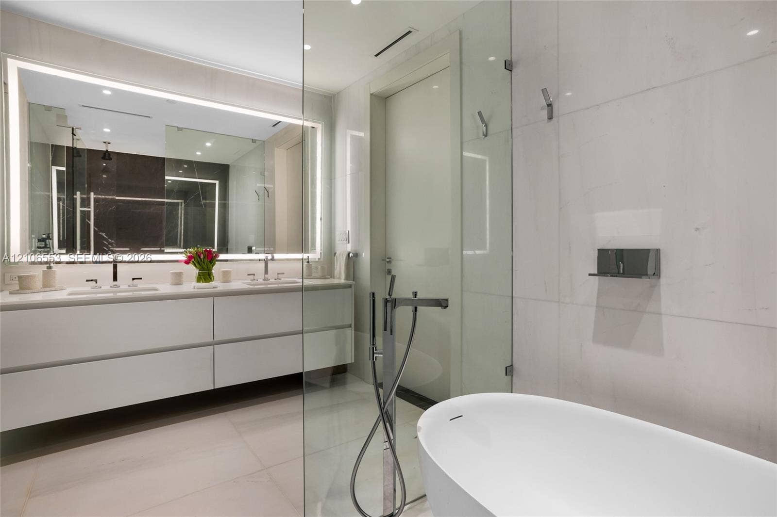 300 Biscayne Boulevard Way, #3002E, Miami, FL 33131 Floating vanity with dual rectangular sinks, oversized backlit mirror, floor-to-ceiling stone wall tiling, glass-enclosed shower, and freestanding soaking tub with floor-mounted faucet
