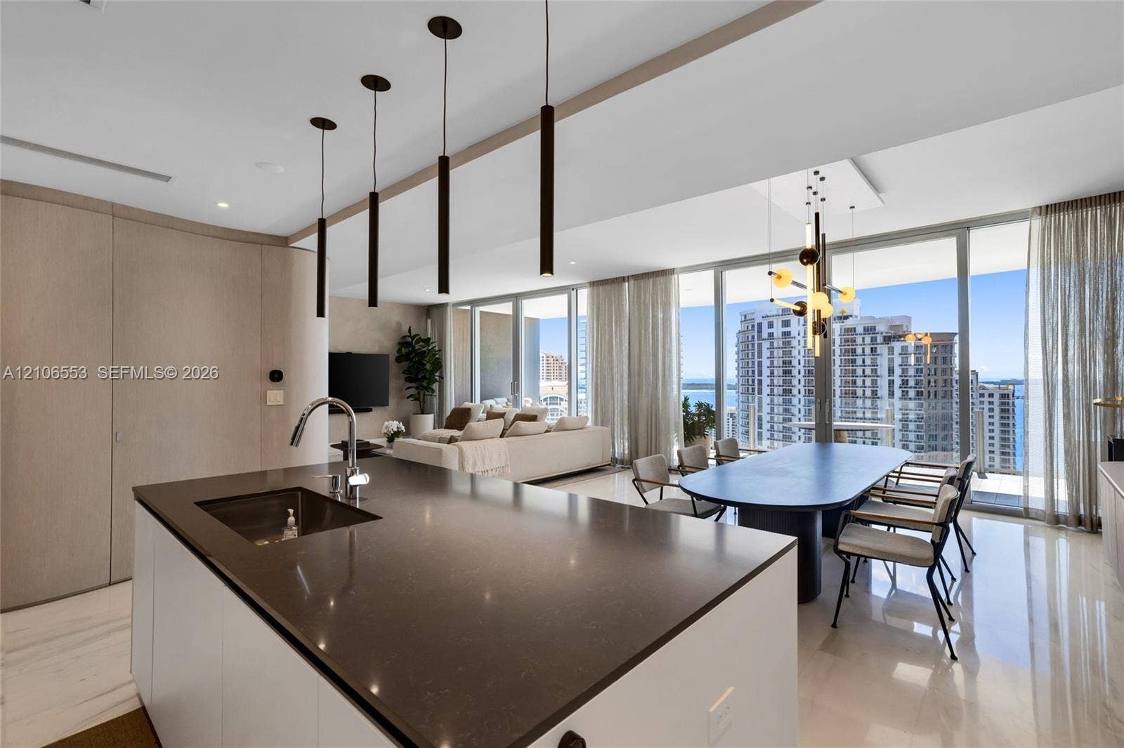 300 Biscayne Boulevard Way, #3002E, Miami, FL 33131 Kitchen island with a dark solid-surface countertop and undermount sink, floor-to-ceiling windows, polished stone flooring, custom cabinetry with integrated paneling, and contemporary multi-pendant lighting