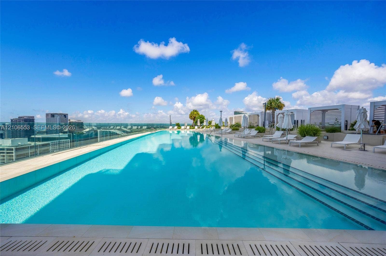 300 Biscayne Boulevard Way, #3002E, Miami, FL 33131 Rooftop infinity-edge pool featuring a glass perimeter railing, submerged tiered steps, and stone-tiled decking