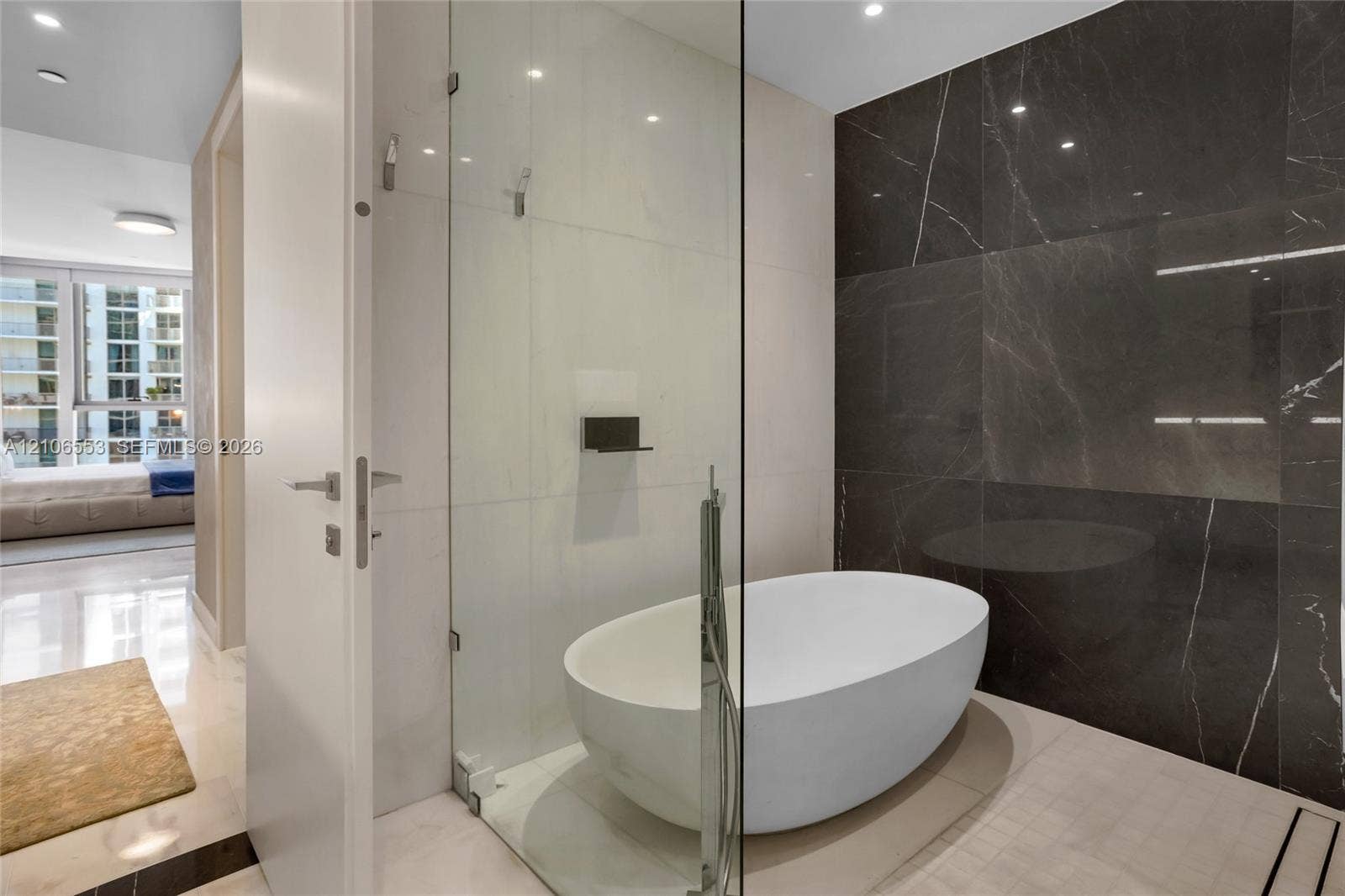300 Biscayne Boulevard Way, #3002E, Miami, FL 33131 Freestanding oval soaking tub enclosed in a glass shower surround, dark stone-finish wall cladding, recessed ceiling lighting, and polished stone-finish flooring
