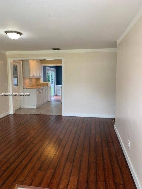 Room featuring wood-finish flooring, neutral wall paint, and crown molding, with a glimpse of a kitchen showcasing white cabinetry and stone countertops