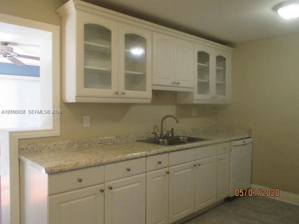 White cabinetry with glass-panel upper doors, stone-finish countertops, stainless steel dual-basin sink, gooseneck faucet, and integrated dishwasher