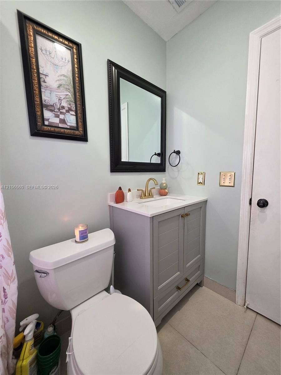 9550 W Elm Lane, Miramar, FL 33025 Grey shaker-style vanity with a stone countertop, integrated undermount sink, brushed gold faucet, and a black-framed mirror