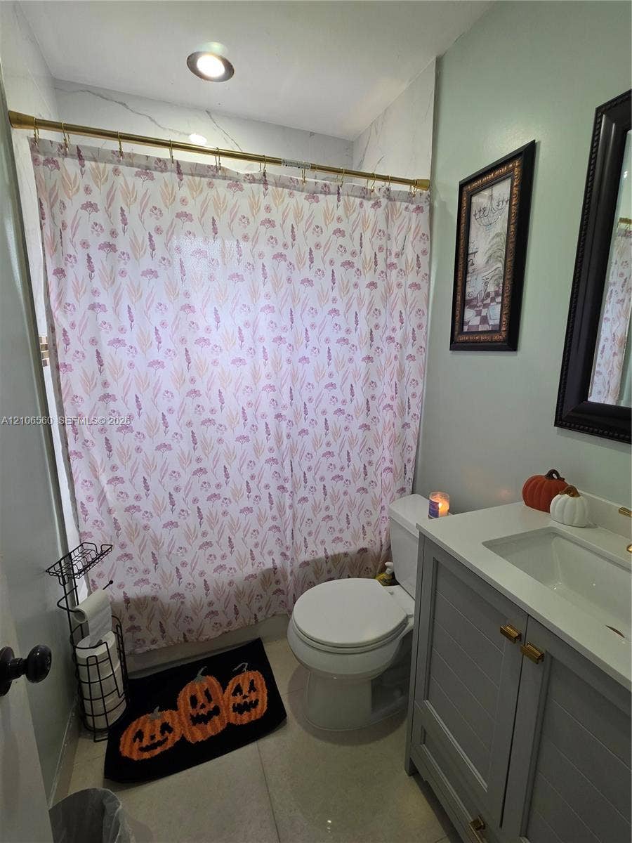 9550 W Elm Lane, Miramar, FL 33025 Grey shaker-style vanity with a solid surface countertop, integrated sink, brass hardware, and a tiled shower surround featuring a brass rod