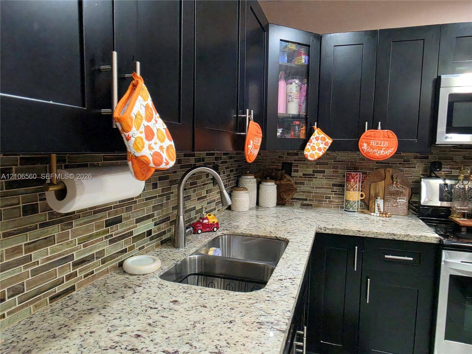 9550 W Elm Lane, Miramar, FL 33025 Kitchen featuring dark shaker-style cabinetry, natural stone countertops, a multi-tonal linear tile backsplash, stainless steel double-basin sink with a gooseneck faucet, and an integrated microwave