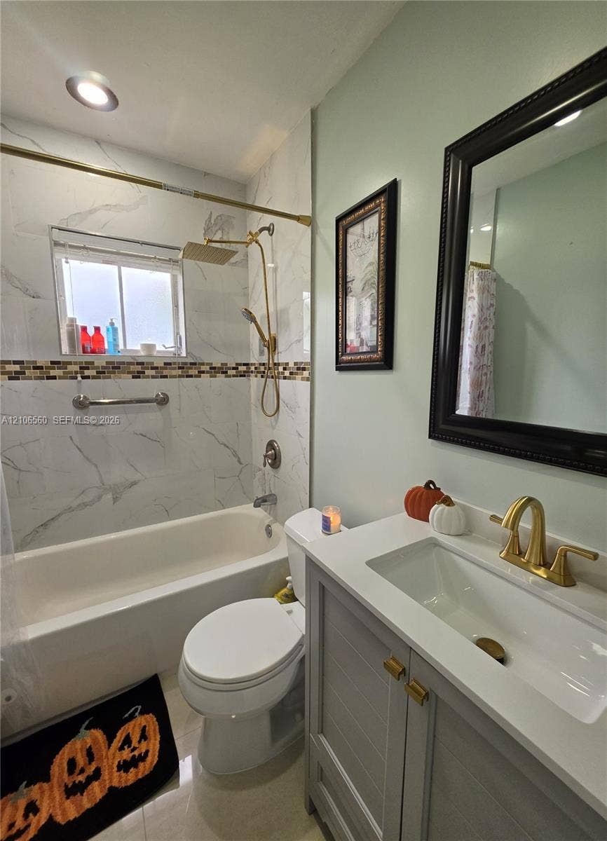 9550 W Elm Lane, Miramar, FL 33025 Bathroom featuring a vanity with a white countertop and gold-toned faucet, large-format tile shower surround with decorative mosaic inlay, gold-toned rainfall shower fixture, and recessed lighting