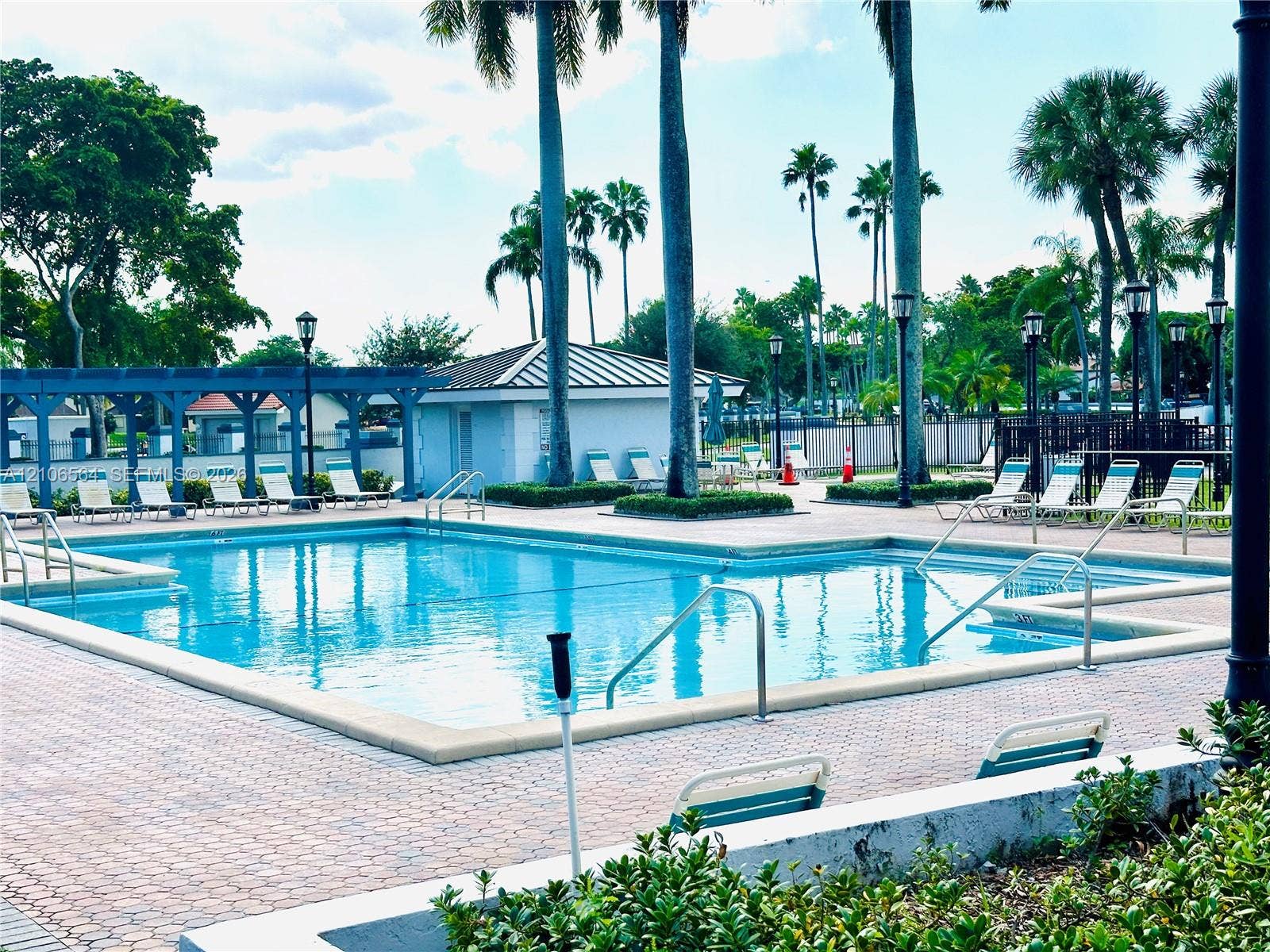 Outdoor swimming pool featuring a brick paver deck, metal pool ladders, a pergola structure, and ornamental street-style lighting