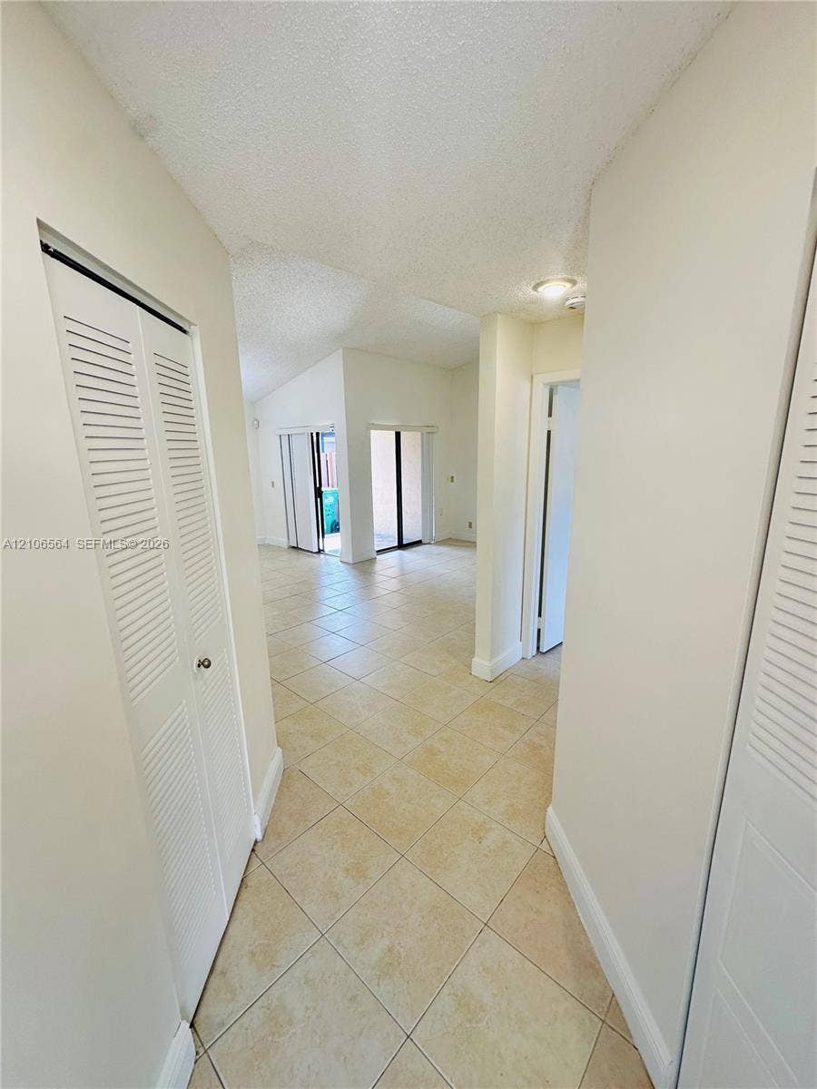 Interior hallway featuring square tile flooring, dual louvered closet doors, and sliding glass doors